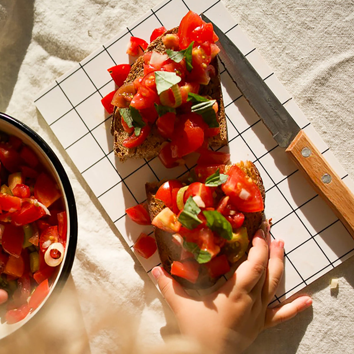 Bruschetta mit Tomaten auf dem weißen Gitter-Brettchen, daneben ein Messer