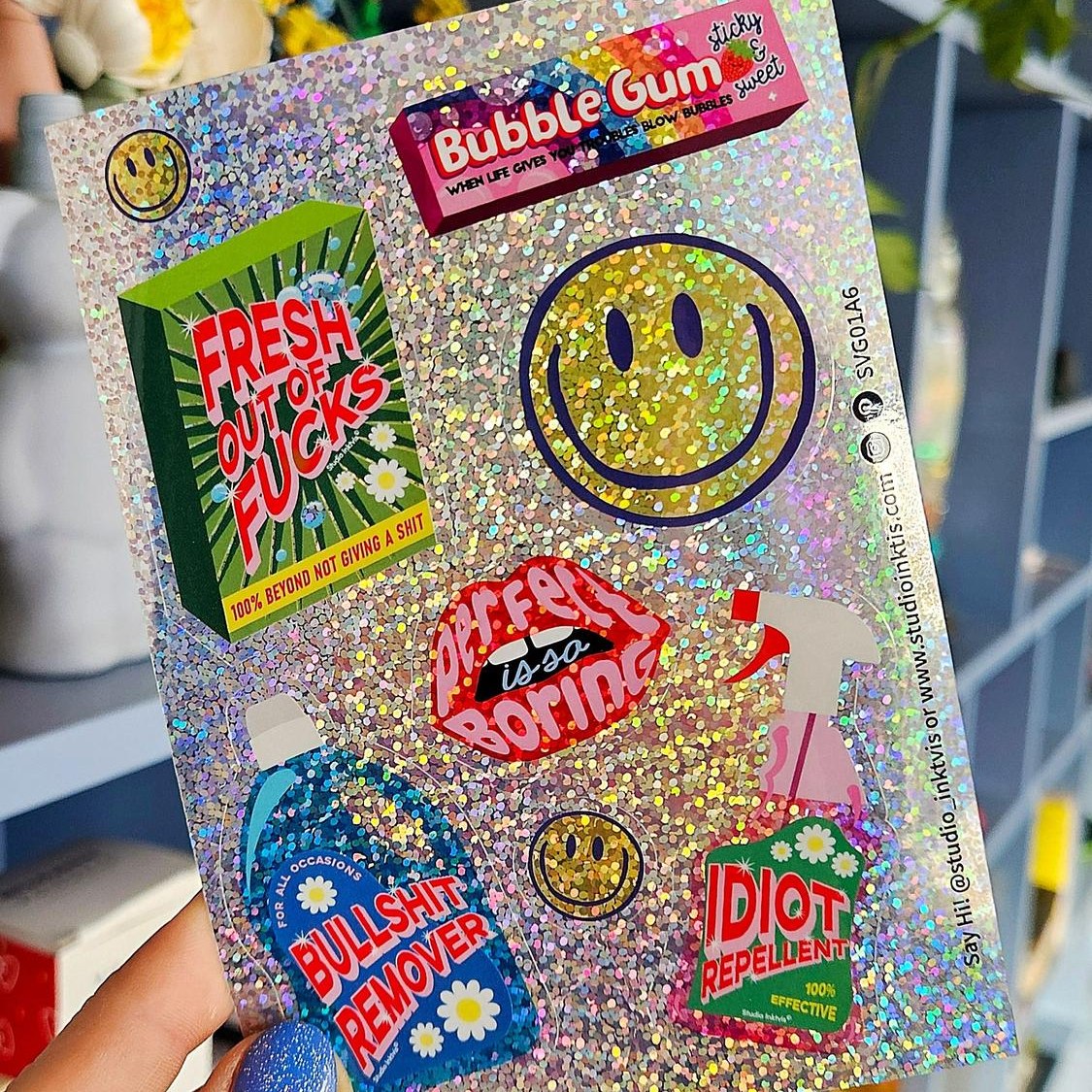 Glitzer-Stickerbogen mit Smiley und Sprüchen in der Hand vor einem Regal