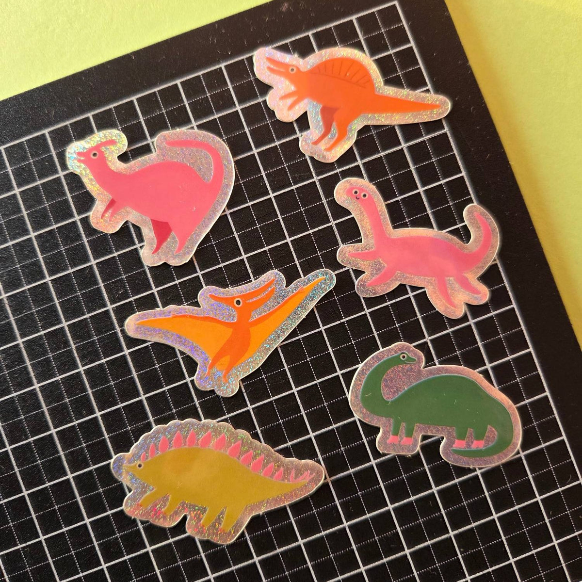 Sechs Glitzer-Dino-Sticker auf schwarzer Schneidematte