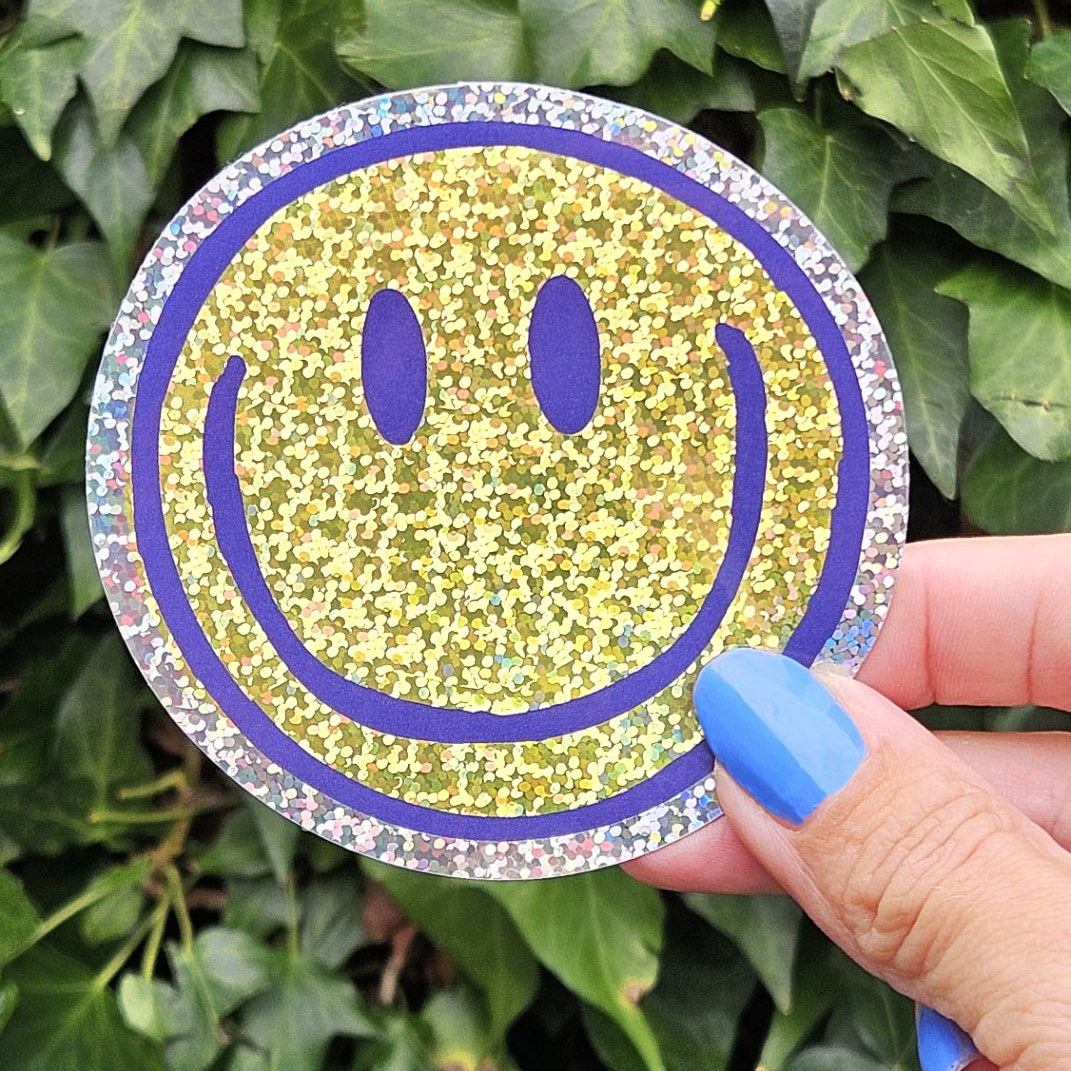 Glitzersticker Smiley in der Hand vor Efeu