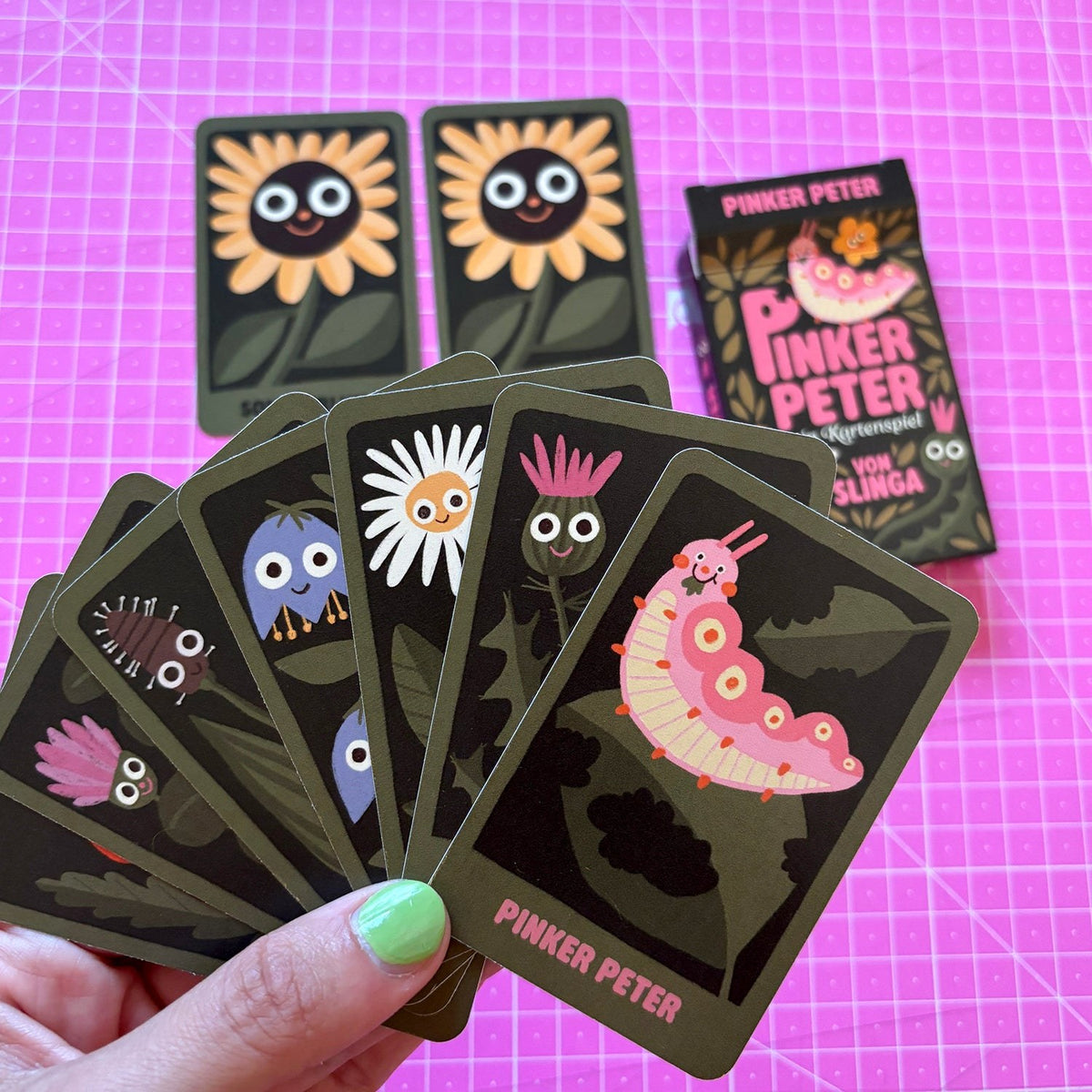 Spielkarten mit Blumen und Raupe in der Hand