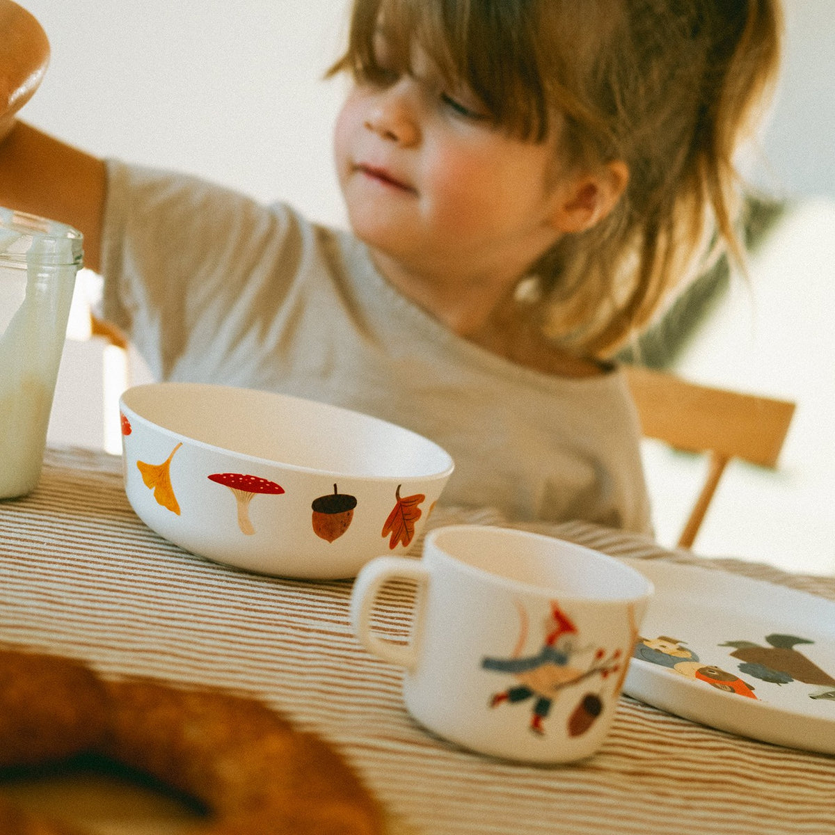 Kind am Frühstückstisch mit Schüssel und Tasse Waldtiere