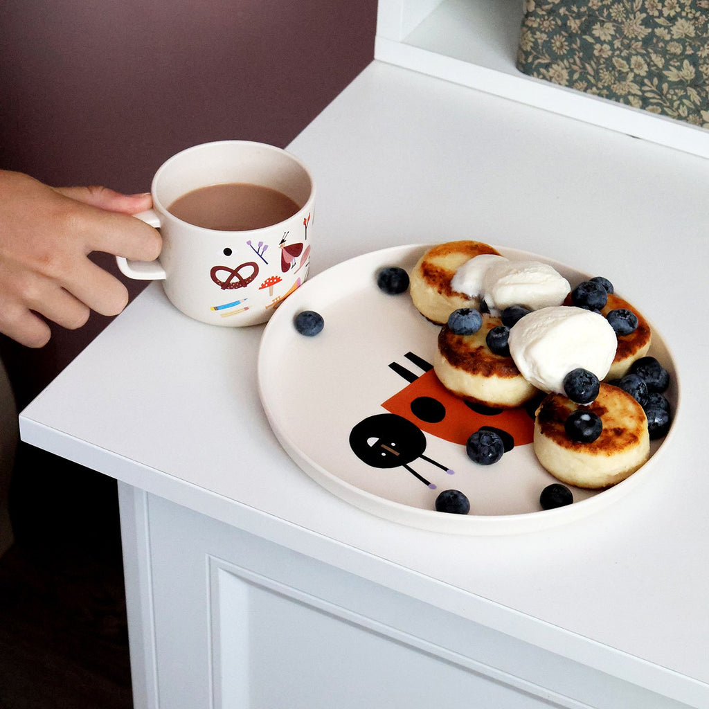 Kinderhand an der Tasse mit Kakao neben Pfannkuchen und Blaubeeren