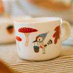 Kindertasse Waldtiere mit Vogel und Fliegenpilz auf einem gestreiften Tischtuch