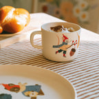 Kindertasse mit Maus auf Schlittschuhen auf dem Frühstückstisch
