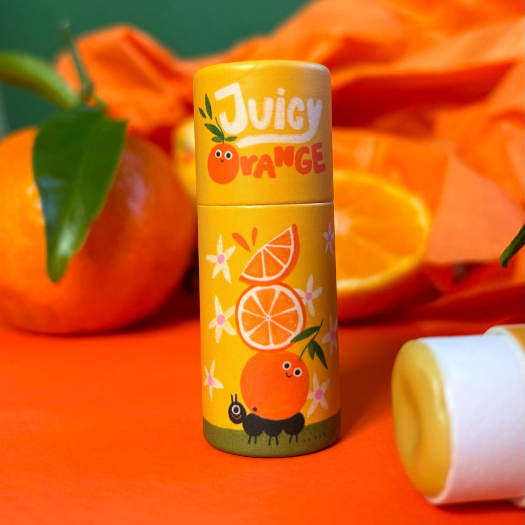 Gelbe Lippenbalsam-Hülse Juicy Orange vor Orangen