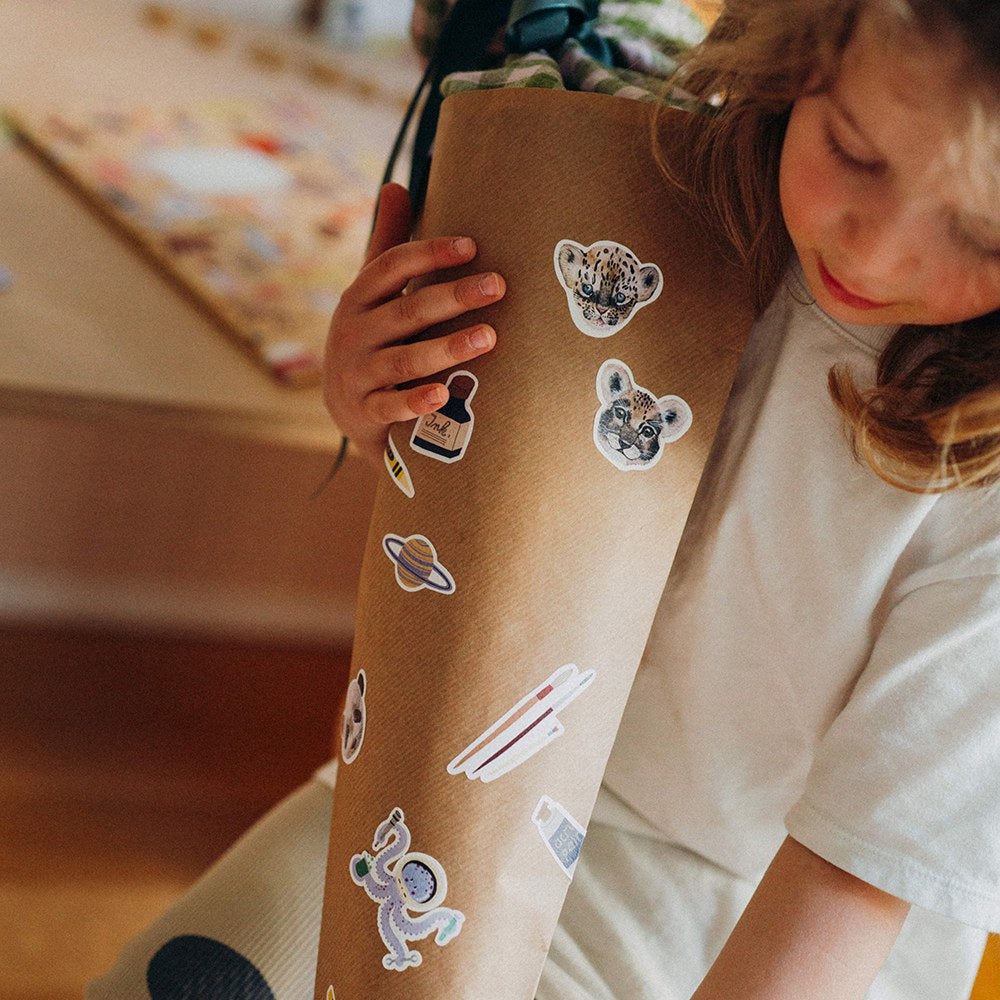Kind beklebt eine Schultüte aus Packpapier mit Weltraum-Stickern