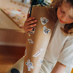 Kind beklebt eine Schultüte aus Packpapier mit Weltraum-Stickern