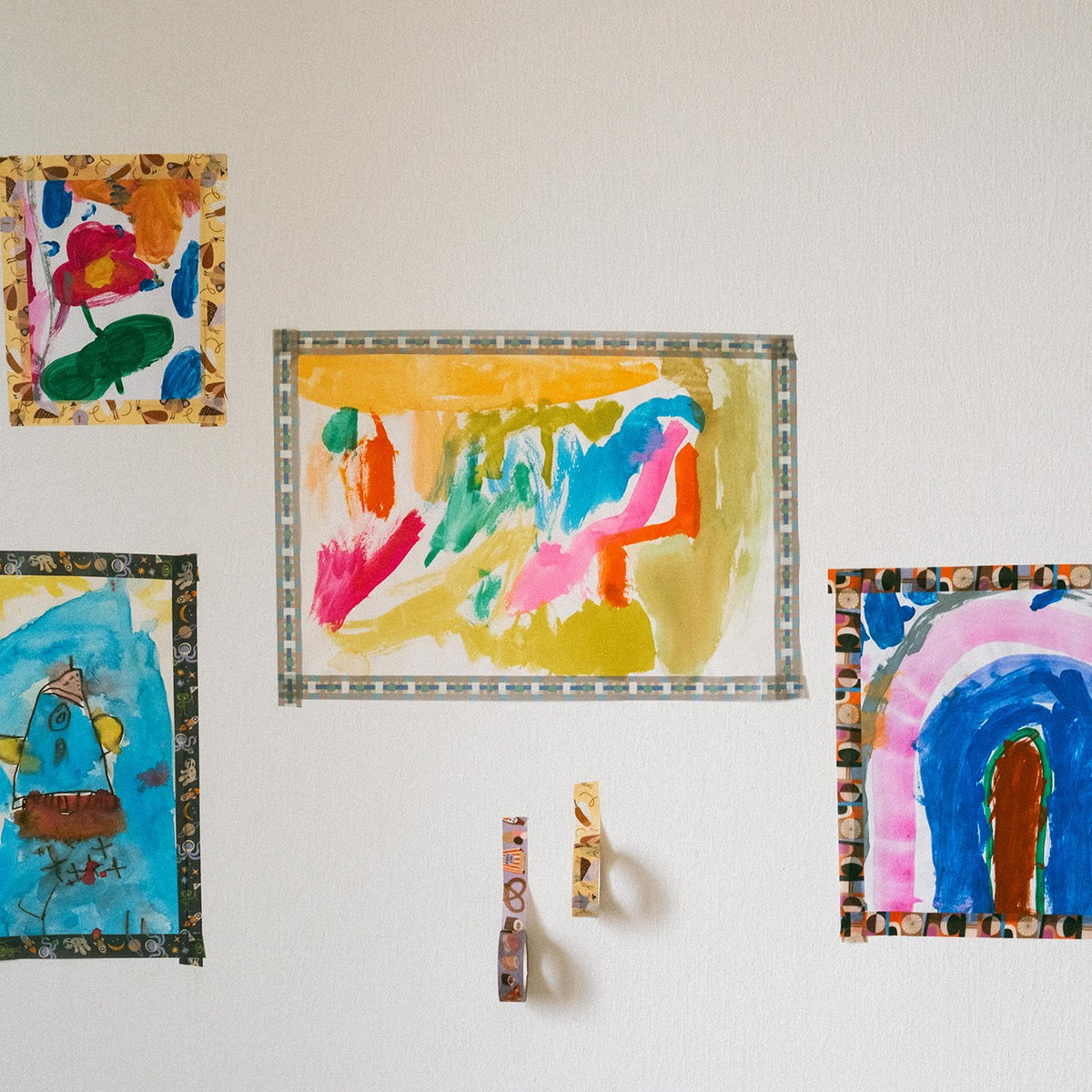 Kinderbilder mit Washi Tape an der Wand, darunter hängende Tape-Rollen